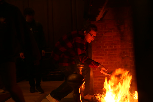 A student throws a sprig of holly onto the fire.
