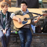 A young man plays his guitar while another enjoys the sounds outside of the Sadler Center on a January day,