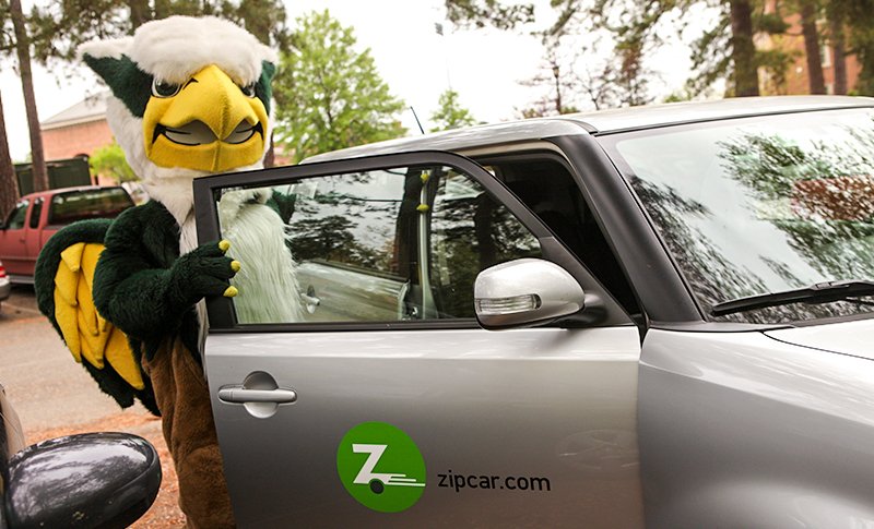 Griffin mascot climbing into a grey vehicle with a Zipcar logo on the door.