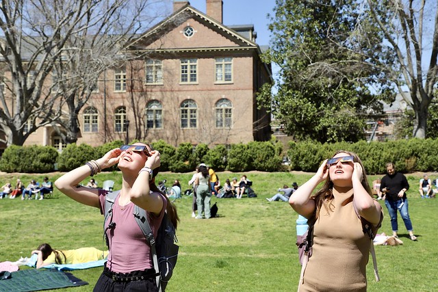 Two students use their special, safety eclipse glasses to catch a glimpse of the solar eclipse from the Sunken Garden.